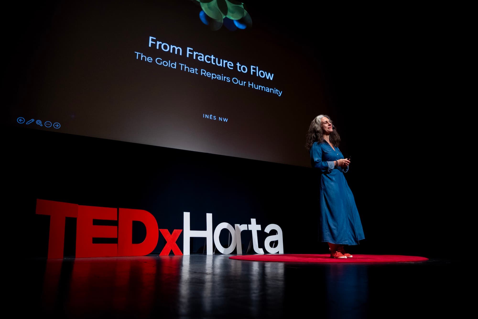 Inês on the TEDxHorta stage, her talk title “From Fracture to Flow” projected behind her