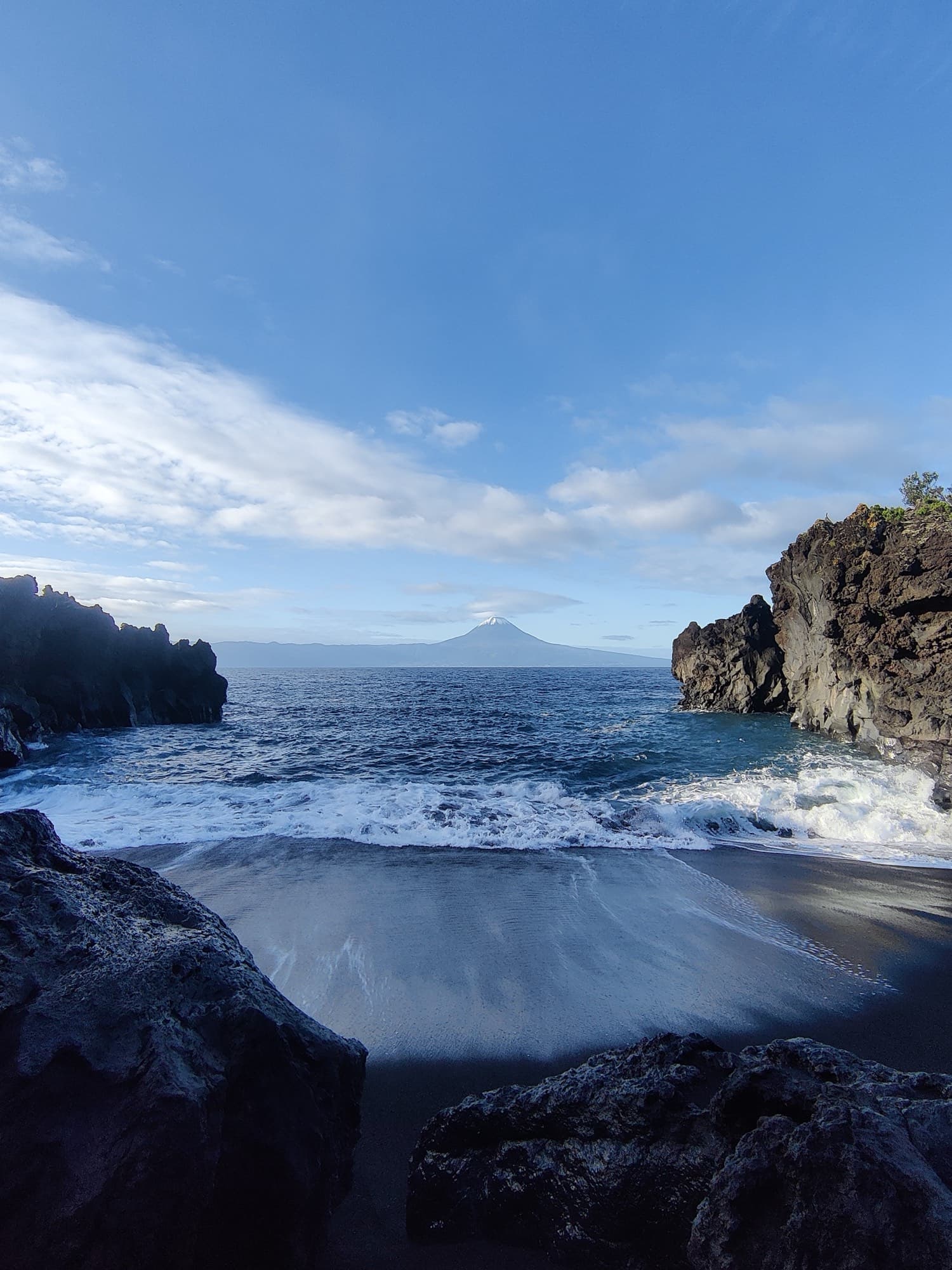 A black sand cove framed by lava rock, Pico across the channel